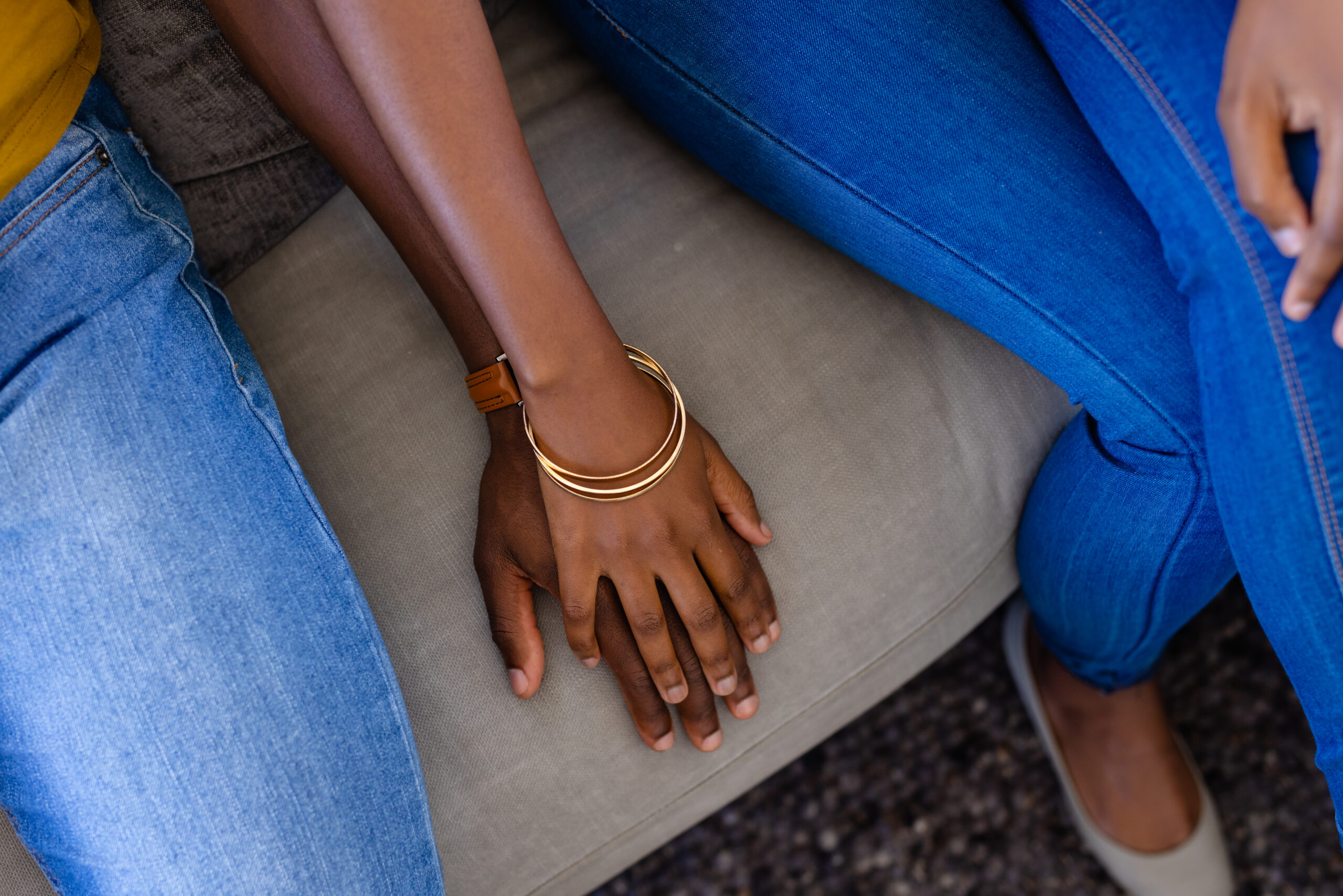 Midsection of african american couple holding hands sitting on couch at home. Love, relationship, wellbeing, happiness and domestic life.